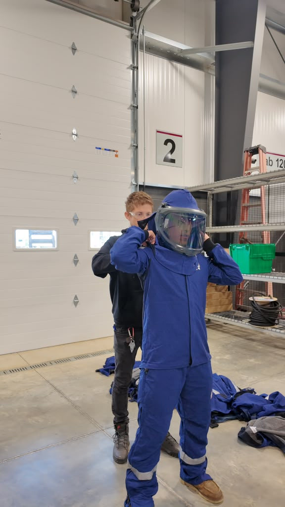 Trainee pulling on the hood of a blue arc-rated flash suit inside the training facility