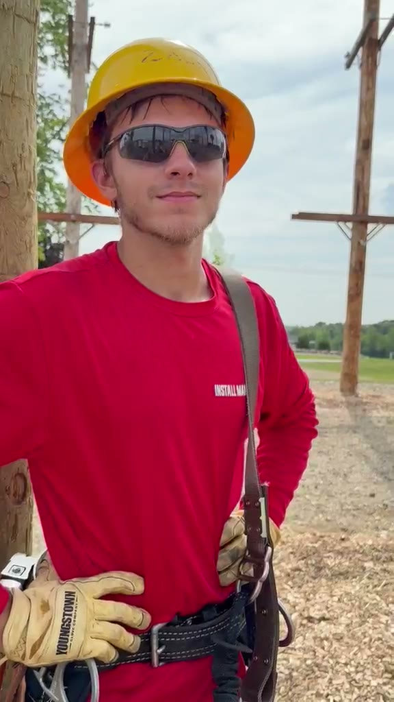 Clip: a student in a hard hat, gloves and climbing belt standing among the poles of the training yard