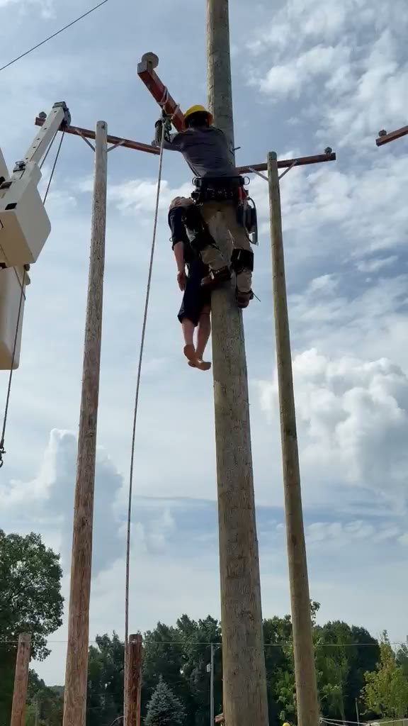 Clip: a lineworker climbing a wooden utility pole outdoors against a bright sky