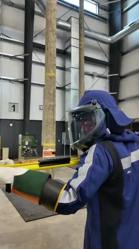 Clip: a trainee in arc-rated PPE approaching a transformer with a hot stick inside the pole-training facility