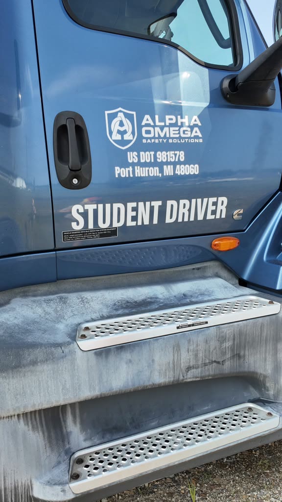 Close-up of a blue CDL training truck door showing the Alpha Omega Safety Solutions logo, US DOT number, and STUDENT DRIVER lettering