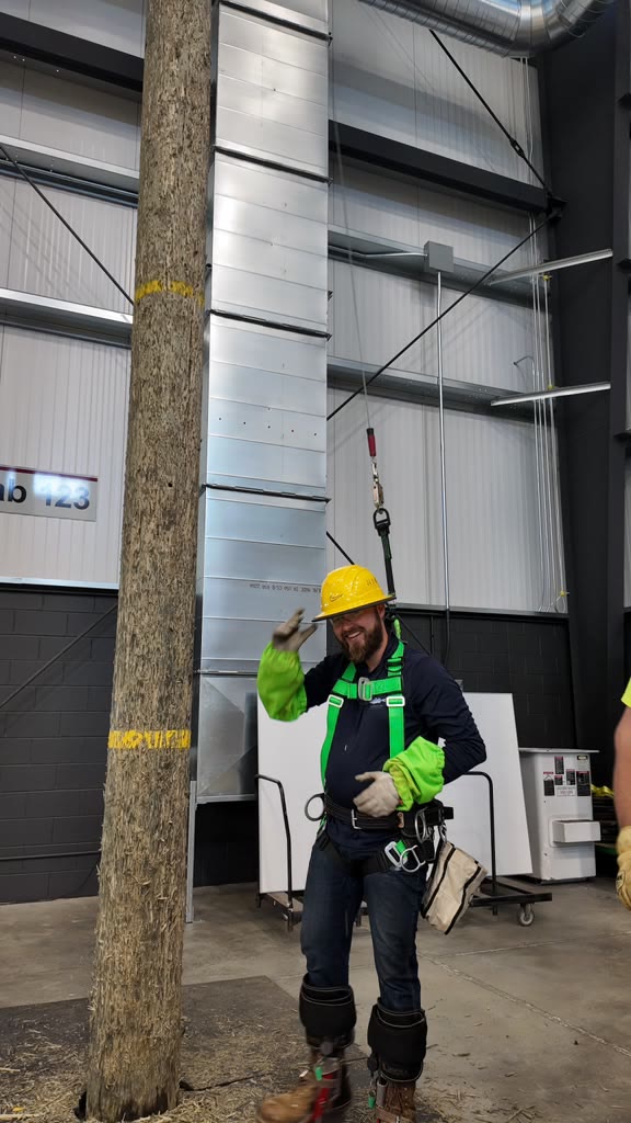 Trainee in a yellow hard hat and harness working on an indoor training pole