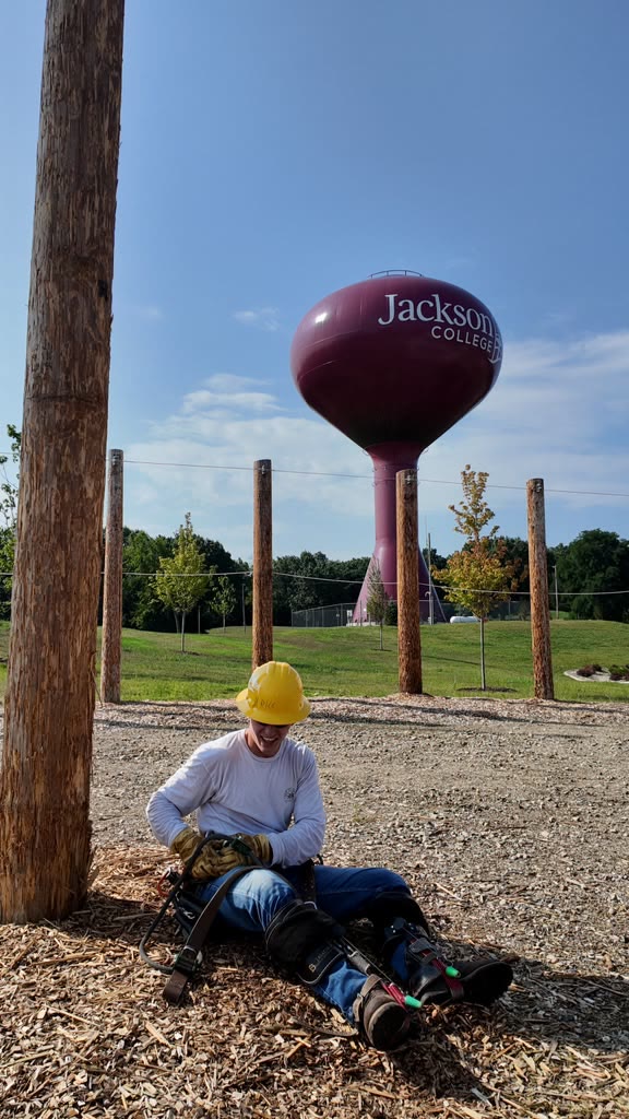 A trainee resting at the base of a training pole with a water tower behind