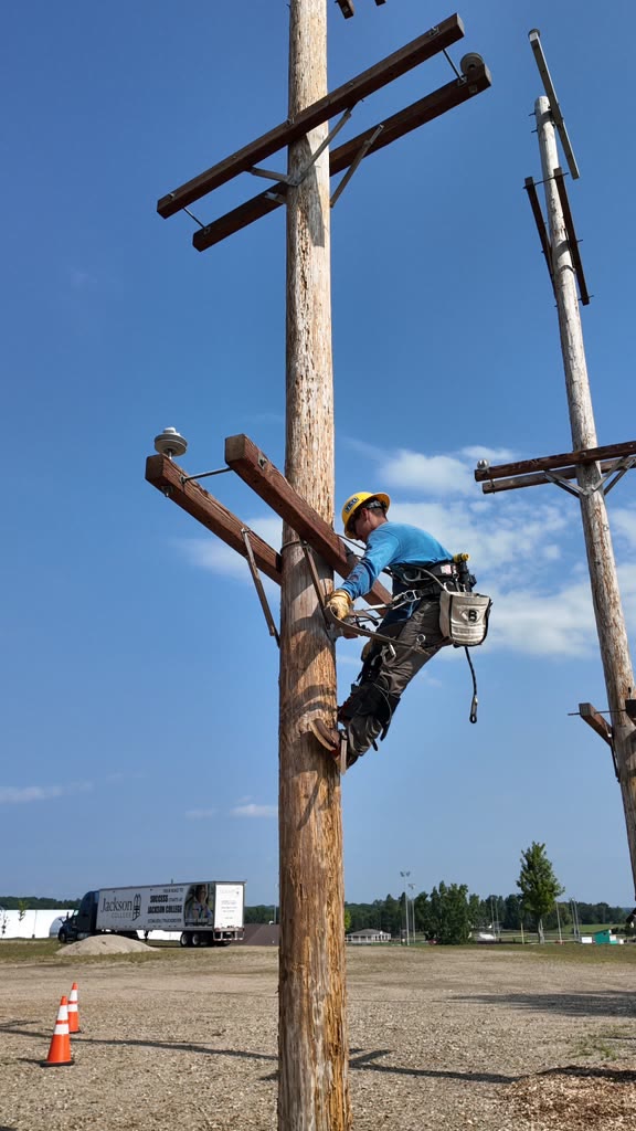 Lineworker working on a crossarm near the top of a utility pole