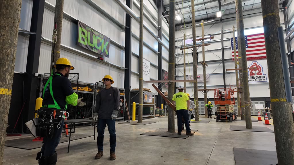 Crew members in hi-vis and hard hats working among poles inside the indoor training facility