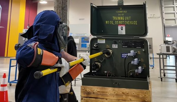 Electrician in full arc-flash PPE operating a hot stick on a padmount training unit